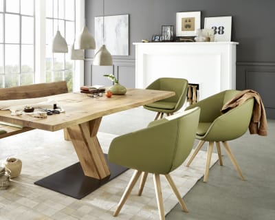 Zeitgenössisches Esszimmer mit dem Wimmer Säulentisch Zweigl Z30 aus Holz, ergänzt durch grüne Stühle und große Fenster. Das Dekor wird durch Hängelampen und gerahmte Kunst aufgewertet.