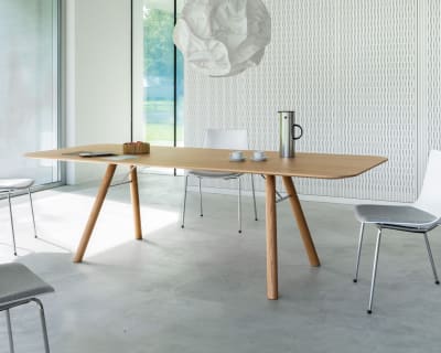 Salle de conférence minimaliste avec table à manger à table en bois Akio, quatre chaises blanches et grandes fenêtres avec vue sur la campagne.