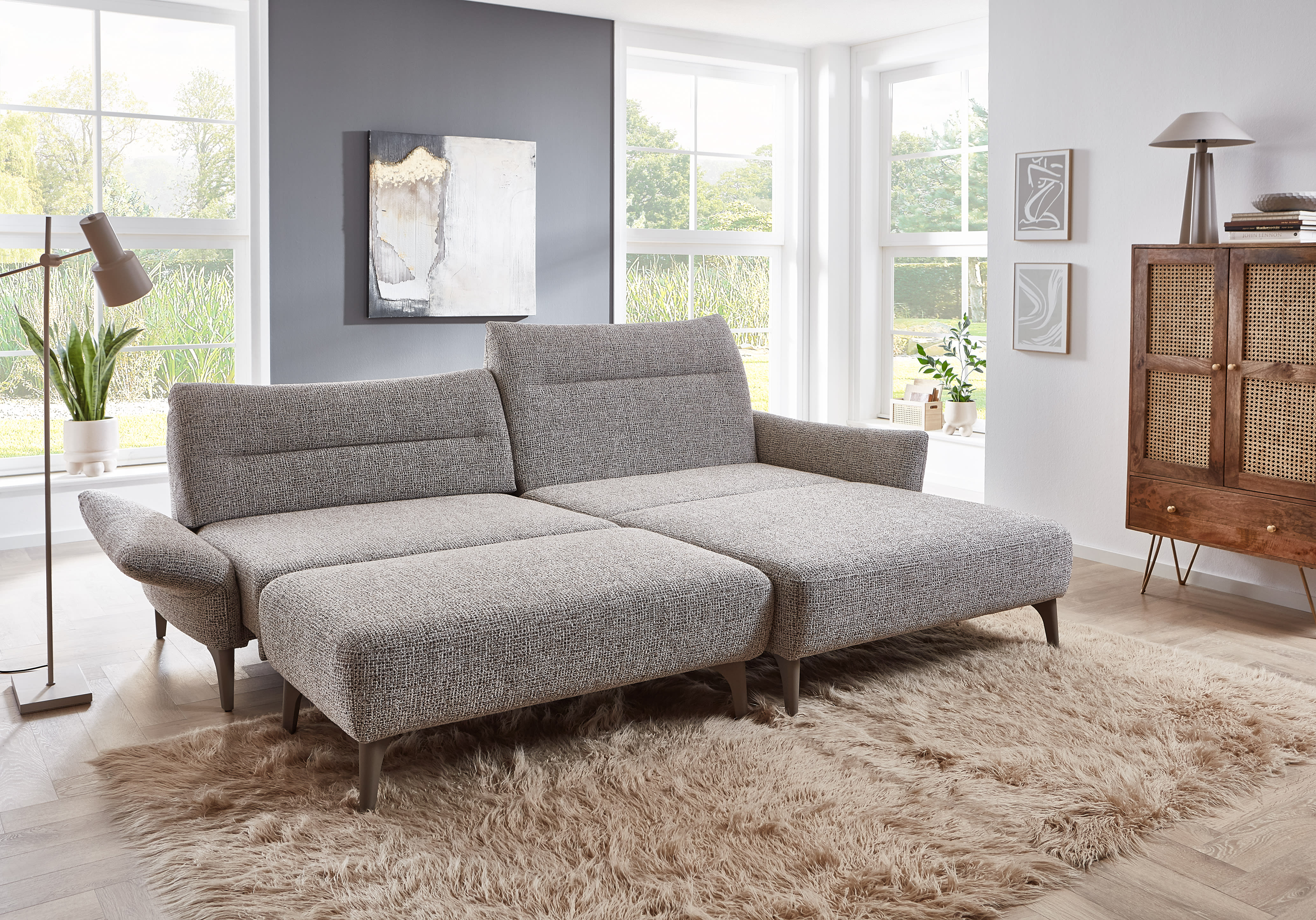 Das Ponsel Sofa Paula mit verstellbaren Sitzen steht auf einem beigen Zottelteppich in einem hellen, modernen Wohnzimmer mit großen Fenstern. Das Ponsel Sofa Paula mit verstellbaren Sitzen steht auf einem beigen Zottelteppich in einem hellen, modernen Wohnzimmer mit großen Fenstern.