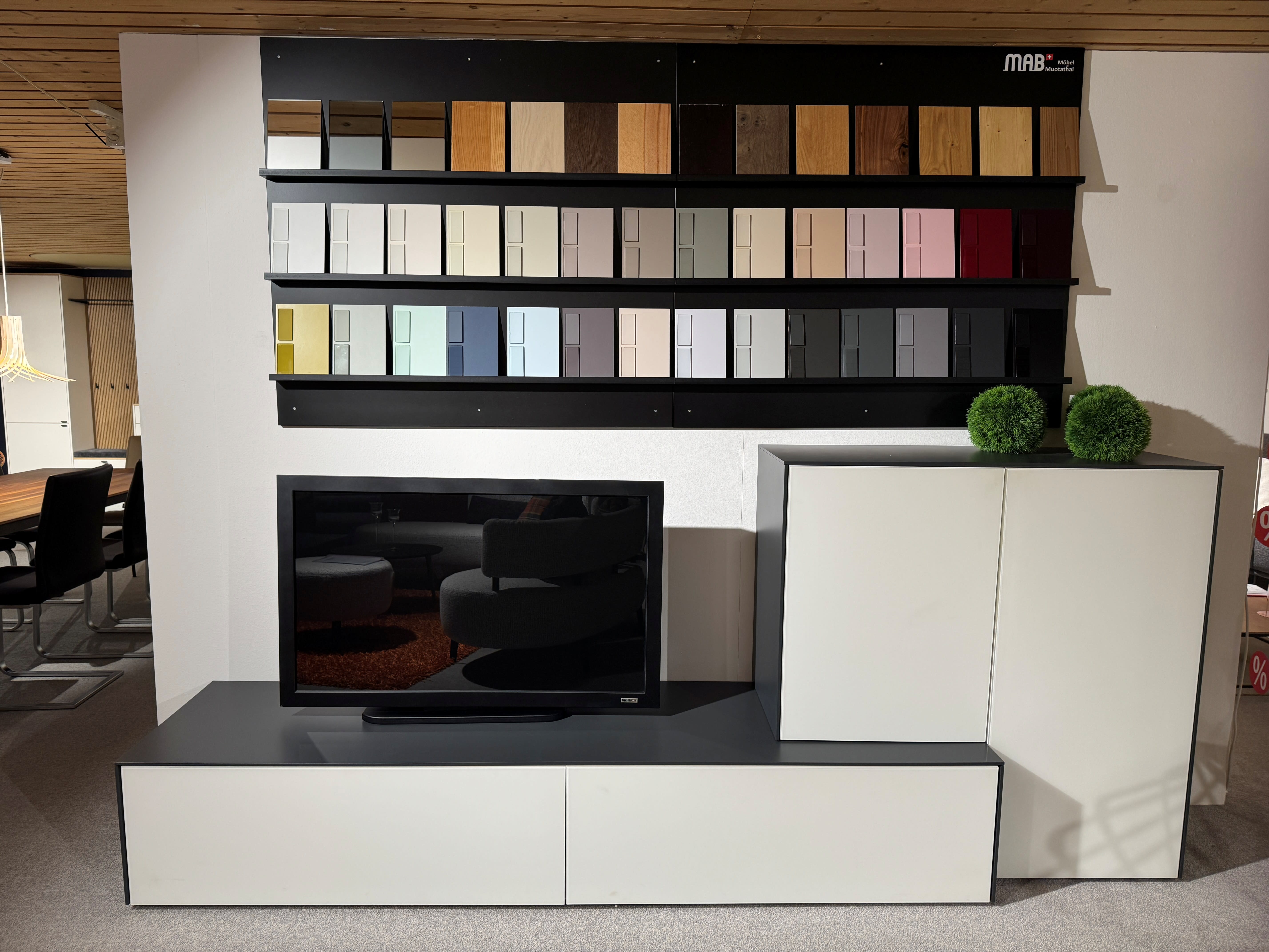 Die MAB TV-Möbel Nara-Konsole besteht aus einem Schrank, zwei grünen Dekokugeln und einem Wanddisplay mit verschiedenen Farbmustern darüber.