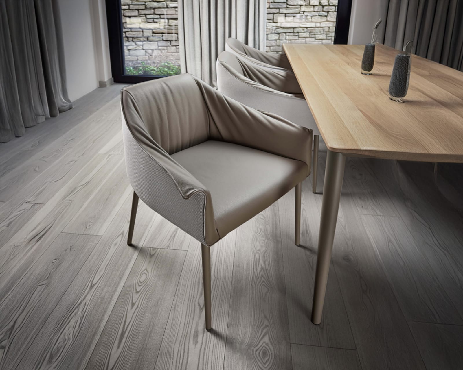 Des chaises rembourrées beiges et une table en bois sur un sol gris clair, à côté de rideaux de fenêtre et devant un mur de pierre en arrière-plan, sont les composants de l&#39;ensemble de table à manger SALE 25 Wimmer Linja L30 incl.
