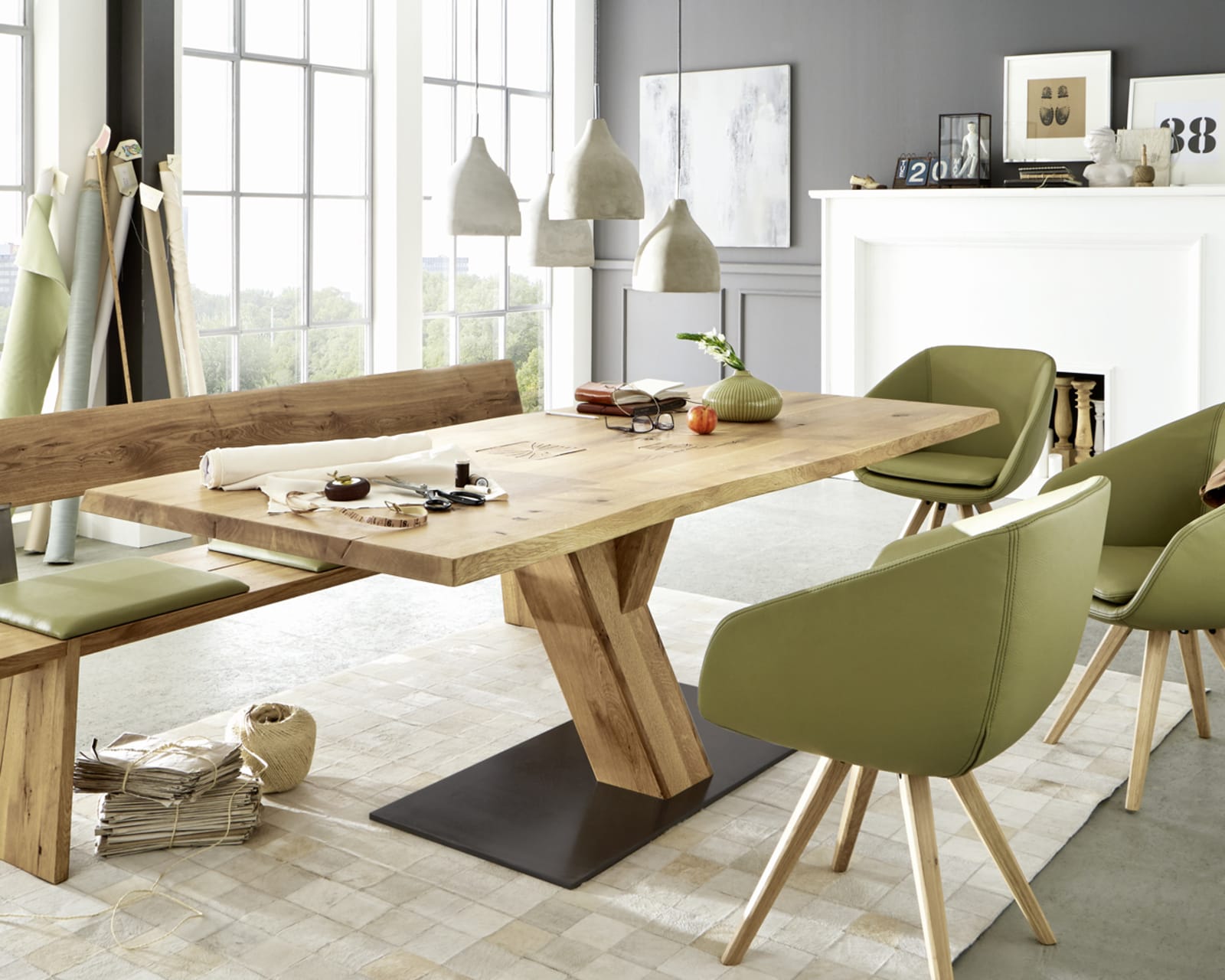 Zeitgenössisches Esszimmer mit dem Wimmer Säulentisch Zweigl Z30 aus Holz, ergänzt durch grüne Stühle und große Fenster. Das Dekor wird durch Hängelampen und gerahmte Kunst aufgewertet.