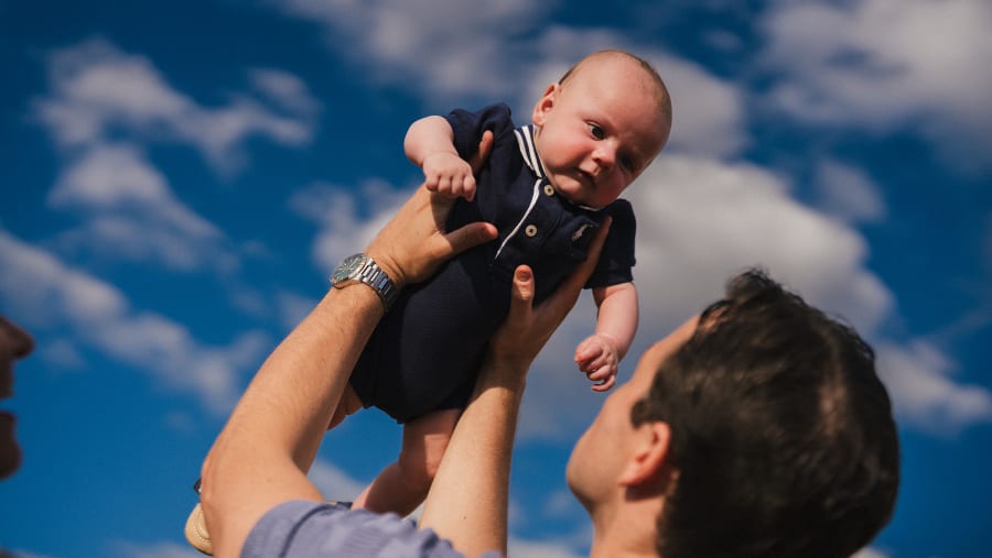 Father lifting his baby into a blue sky