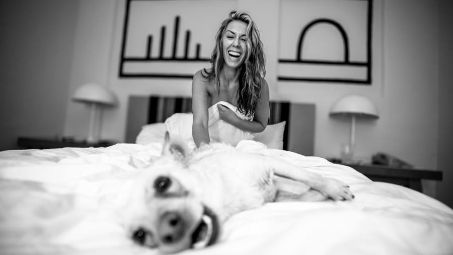 Woman laughing in bed with her dog, black and white