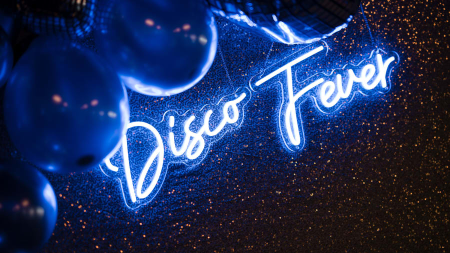 Blue neon Disco Fever sign glowing at a party