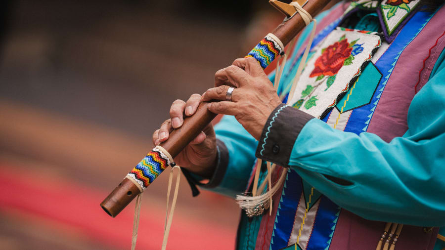 Hands on a beaded wooden flute, turquoise sleeve