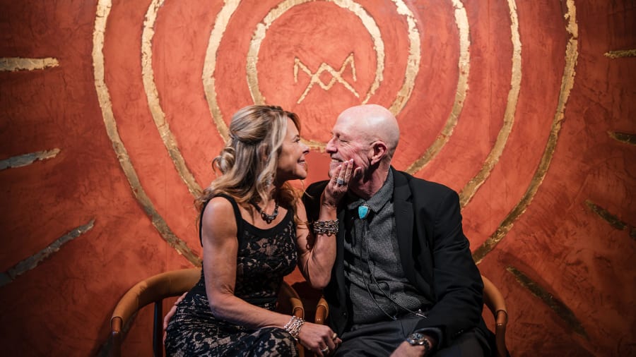 Couple close on a bench in front of a red painted mural
