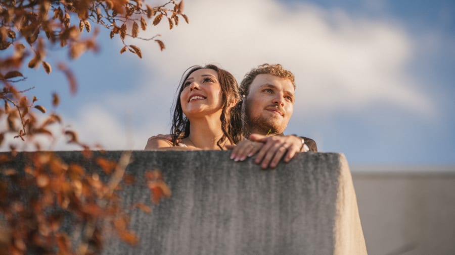 Couple leaning on a sunlit wall under autumn leaves