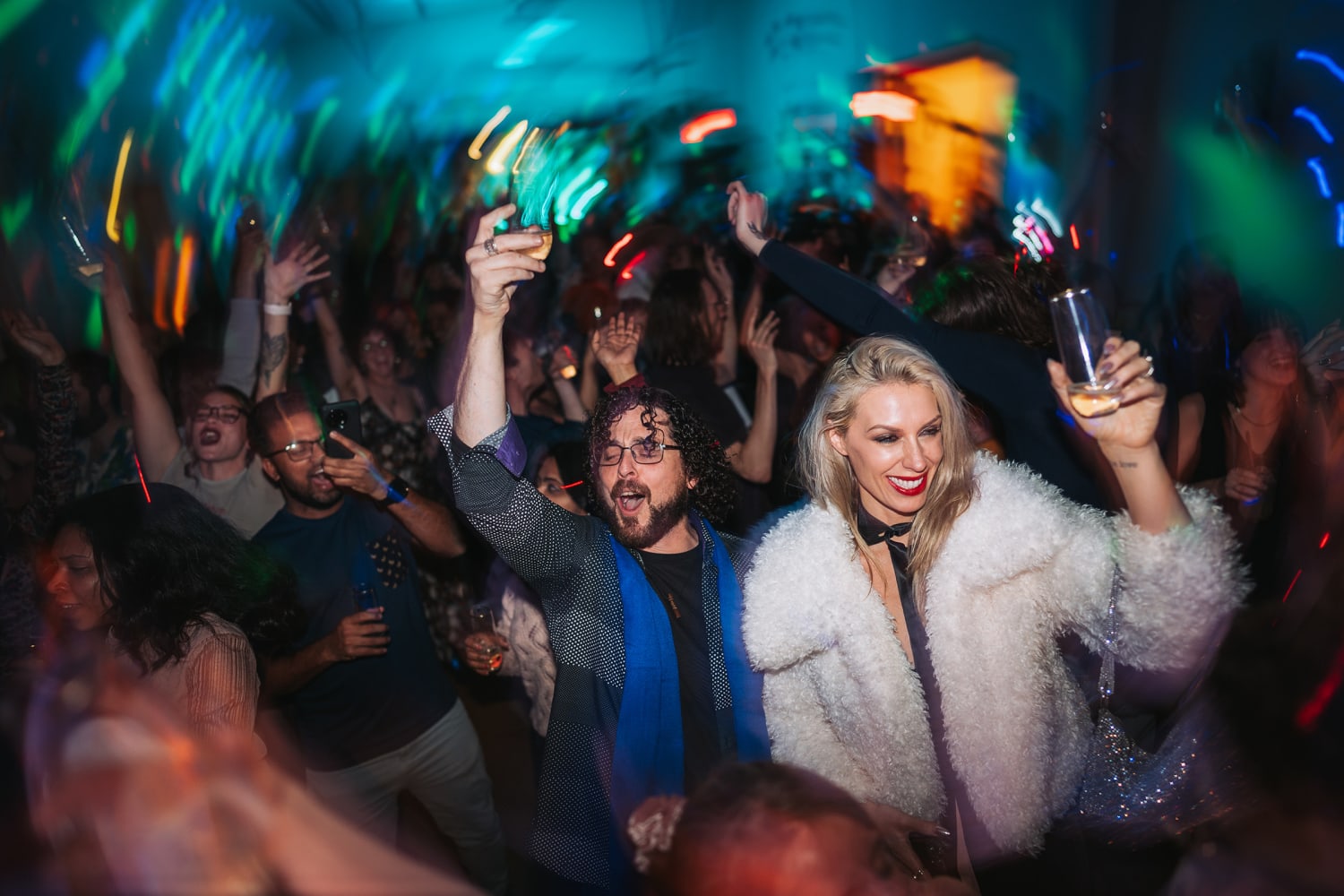 This indoor nightclub scene documents a lively evening celebration with vibrant ambient lighting in teals, greens, oranges, and blues creating a dynamic atmosphere — Casey Addason Photography