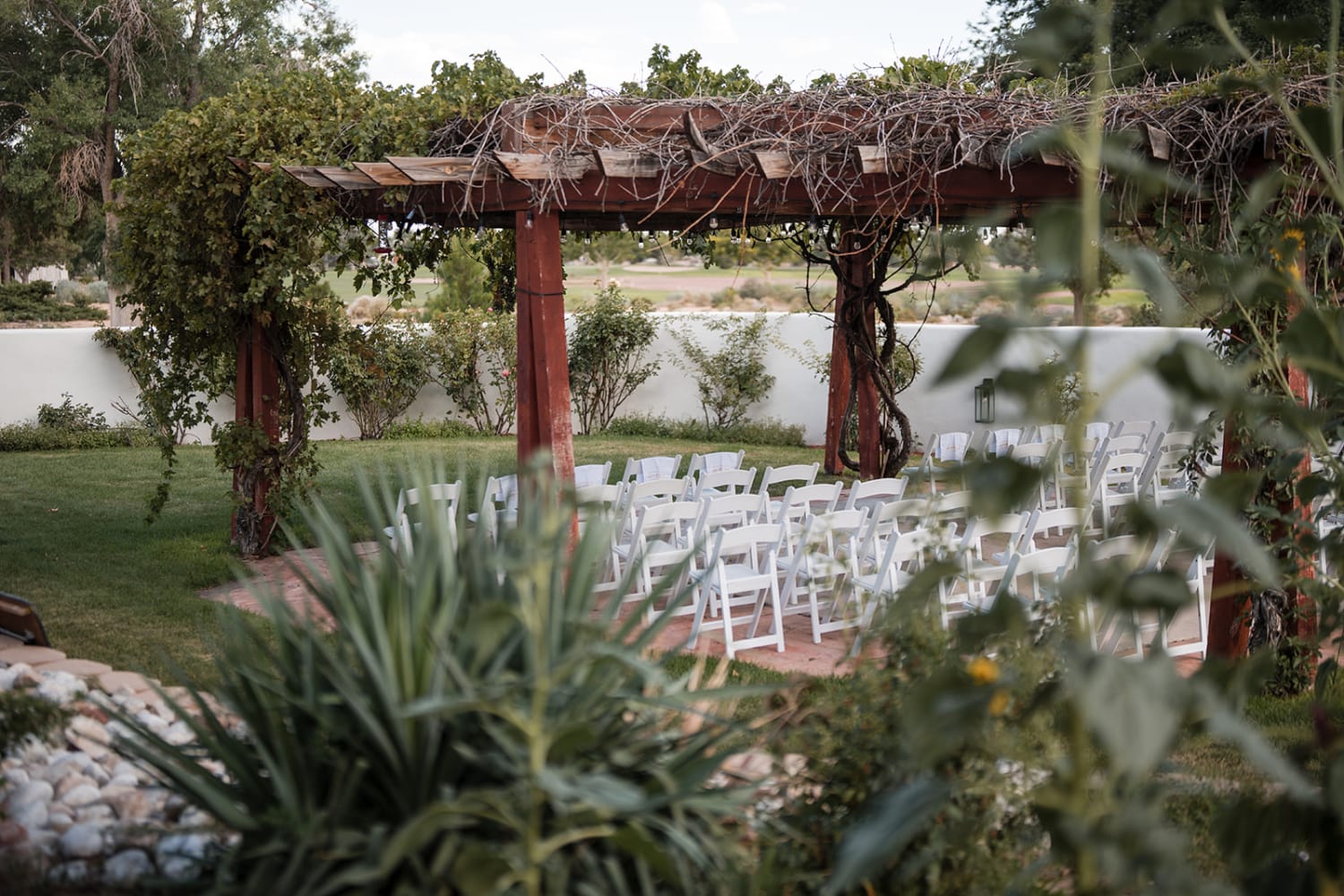 wedding ceremony is set in a landscaped garden venue featuring a rustic wooden pergola with climb... — Casey Addason Photography