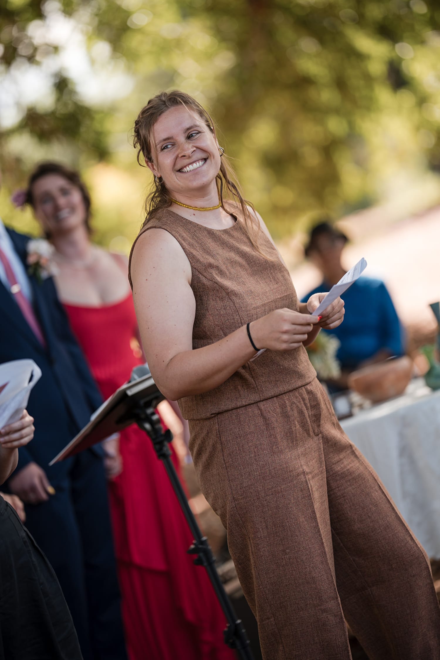 daytime event captures a woman in a brown linen sleeveless dress and gold choker smiling at the c... — Casey Addason Photography