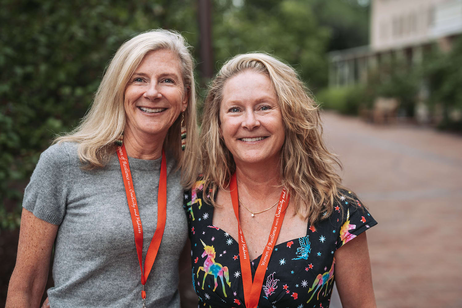Two women pose together outdoors on a brick pathway lined with mature trees and ivy-covered insti... — Casey Addason Photography