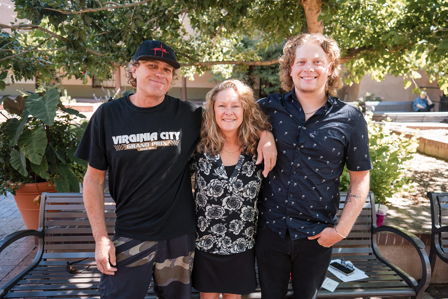 portrait captures three smiling subjects posed on a wooden bench in a sunny courtyard setting, su... — Casey Addason Photography