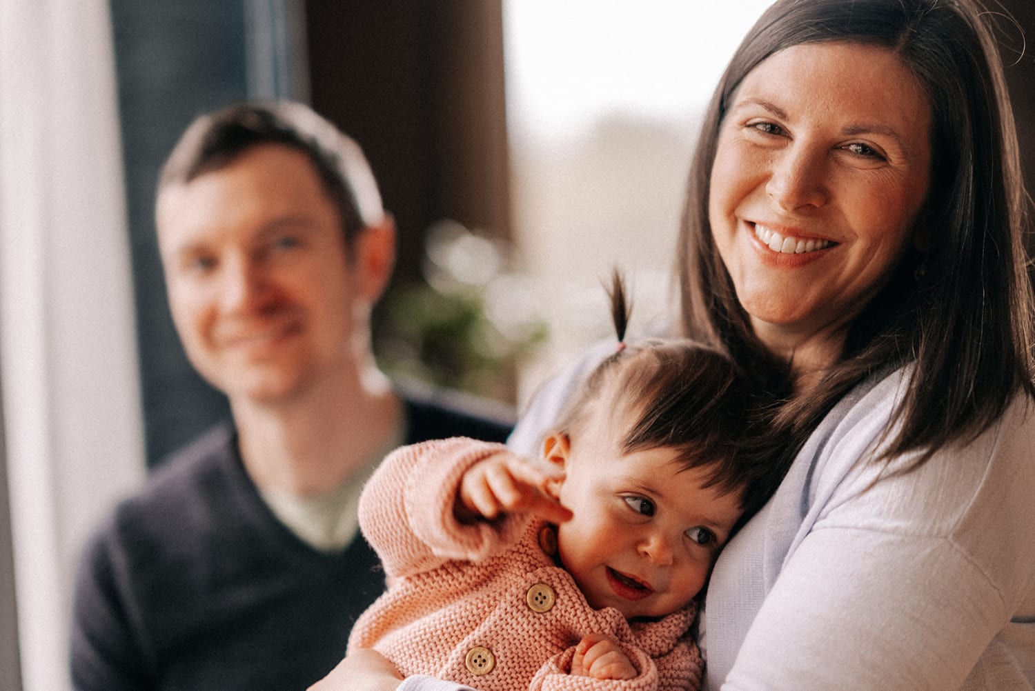 This intimate family portrait photographs a woman holding a baby in a soft pink knitted sweater, with a — Casey Addason Photography