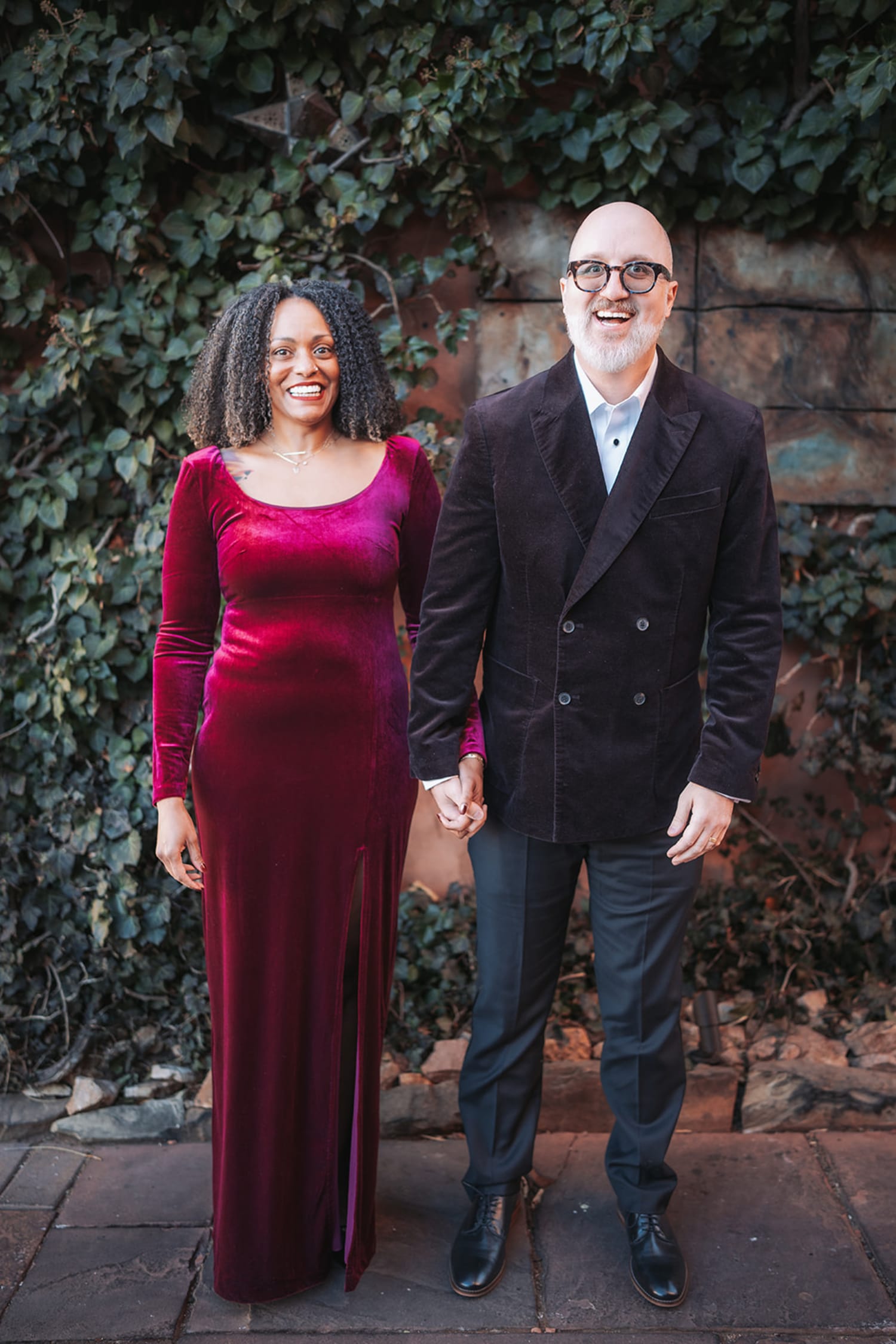 Couple against ivy-covered brick wall at Inn of the Five Graces Santa Fe, magenta velvet gown, charcoal blazer, candid joyful moment, Casey Addason Photography