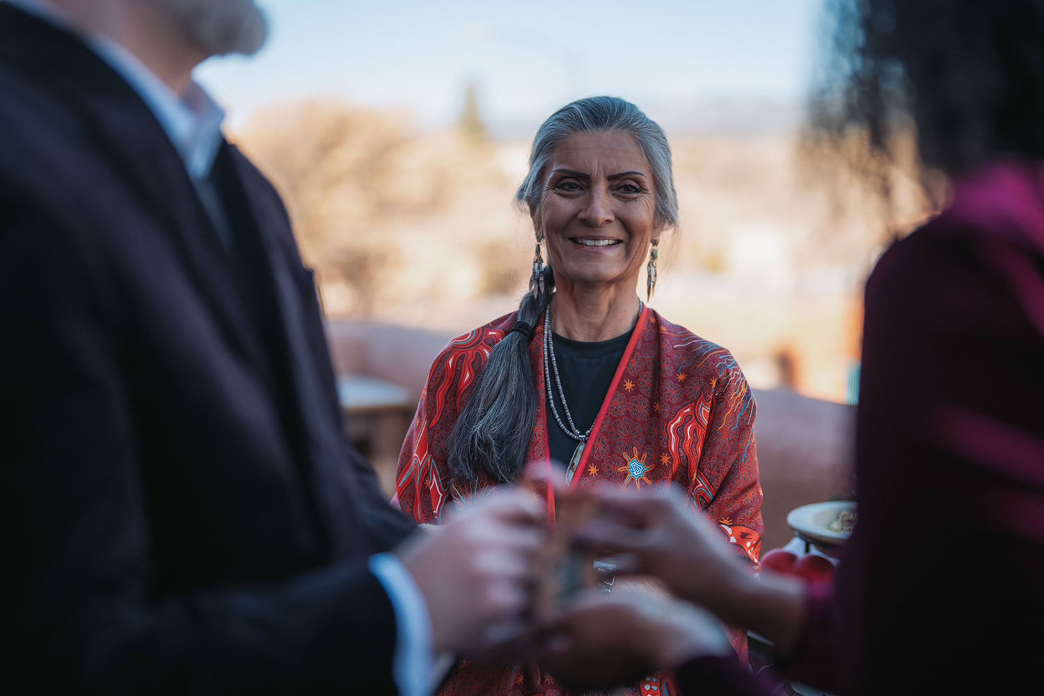 Woman in red patterned jacket with traditional jewelry at Inn of the Five Graces, golden hour desert vista, adobe architecture, cultural celebration, Casey Addason Photography