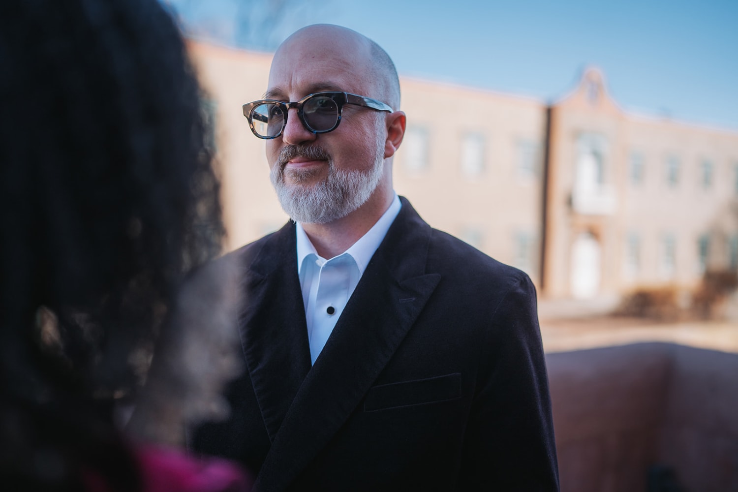 Man in black blazer against adobe buildings at Inn of the Five Graces Santa Fe, golden hour, mature gray beard and glasses, Casey Addason Photography