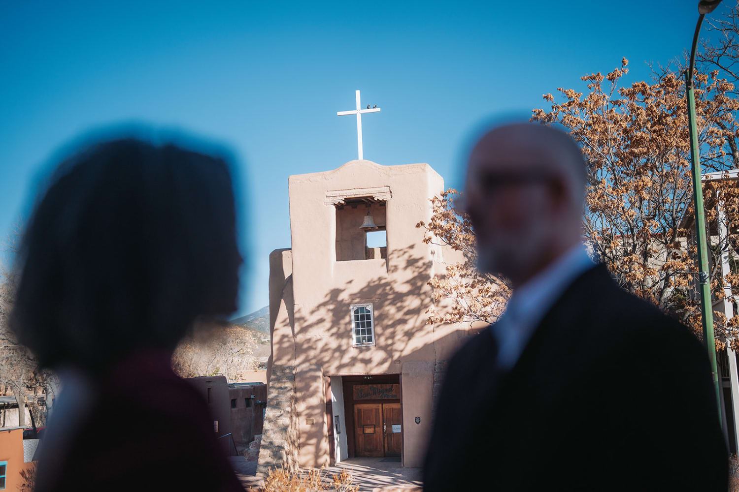 Adobe chapel exterior near Inn of the Five Graces Santa Fe, wooden cross and bell tower, cottonwood trees, golden hour, Casey Addason Photography