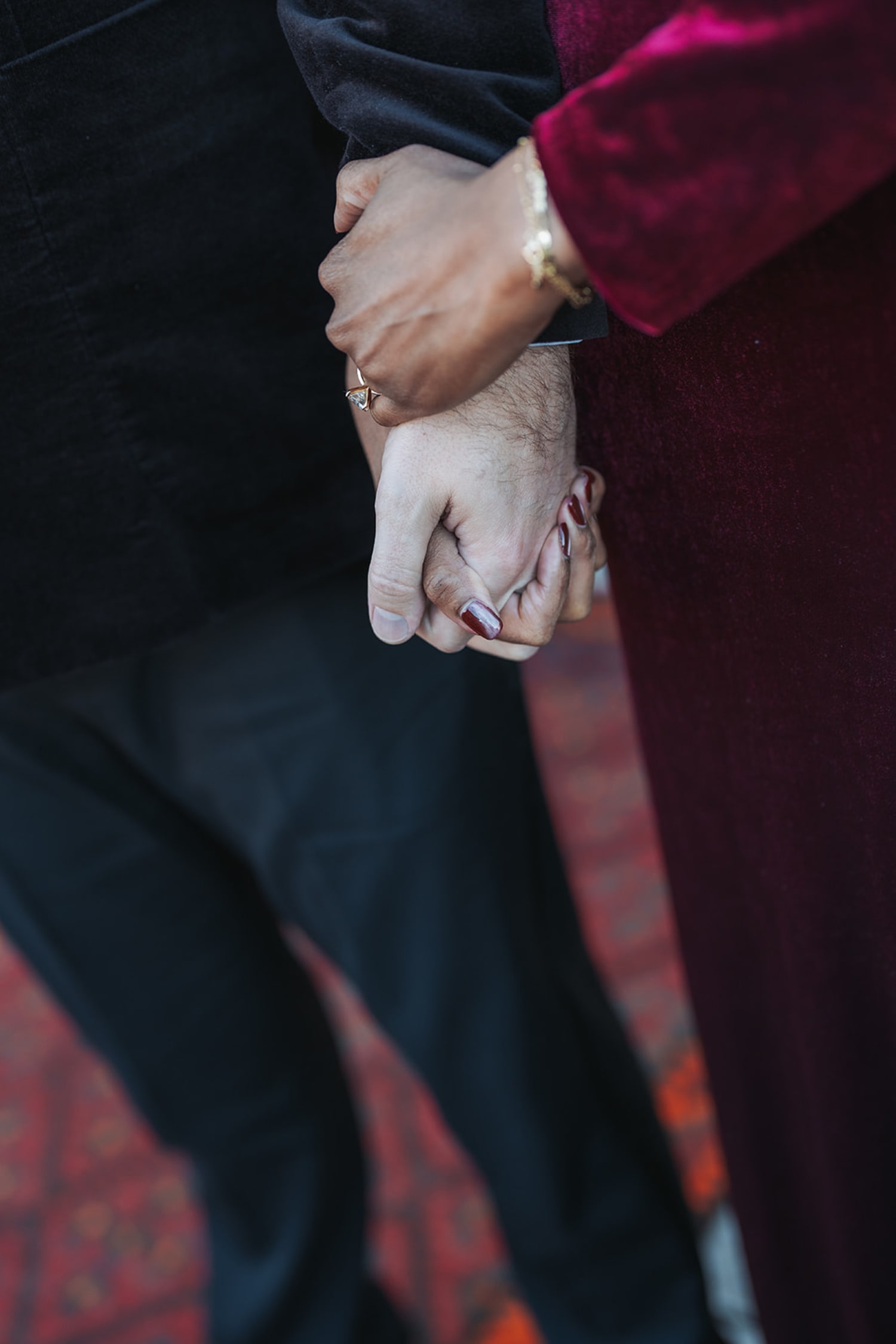 Close-up hands holding at Inn of the Five Graces, burgundy velvet jacket, formal attire with rings and bracelets, warm romantic mood, Casey Addason Photography