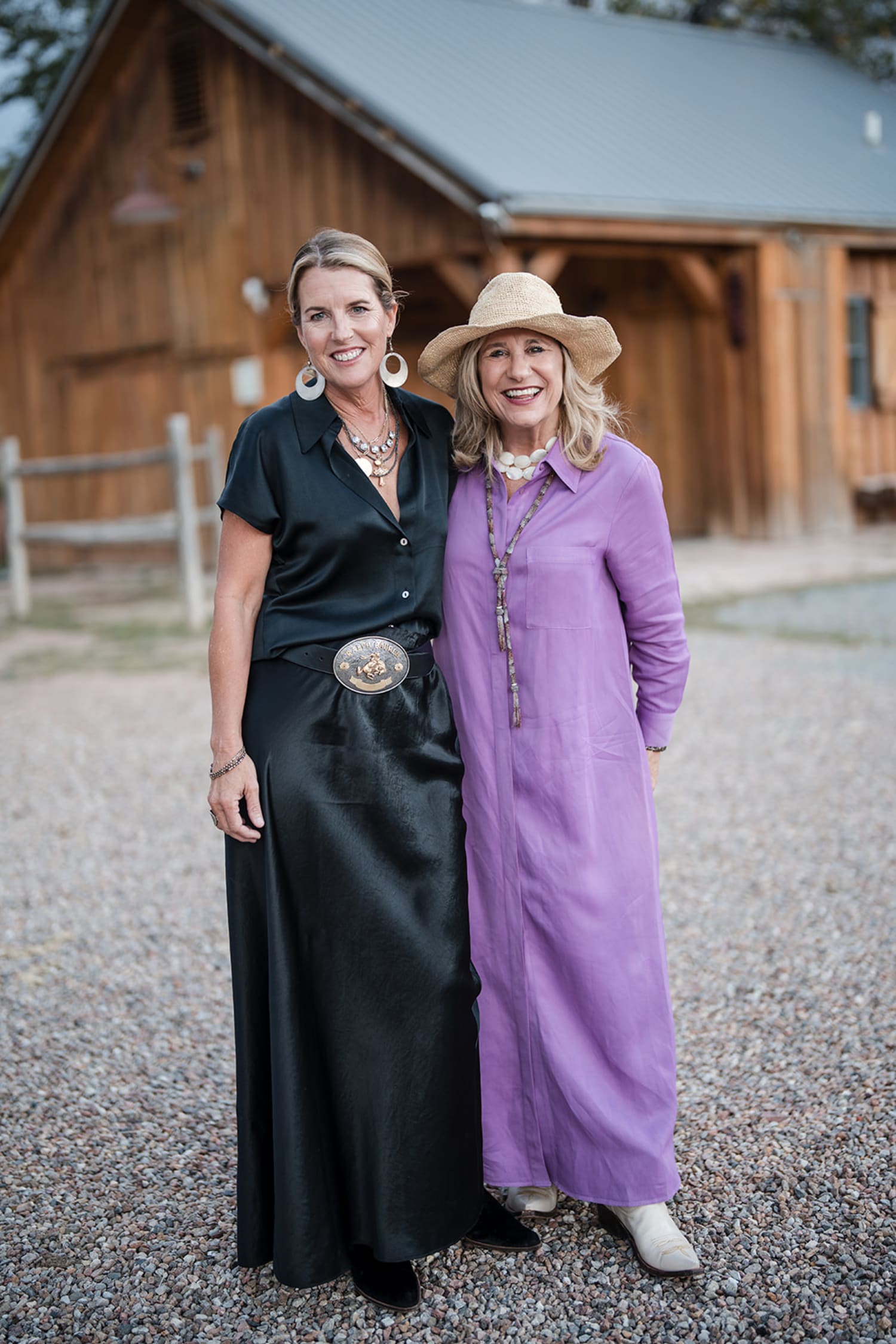 Two women pose together on a gravel driveway at a rustic wooden ranch property, with log cabin st... — Casey Addason Photography