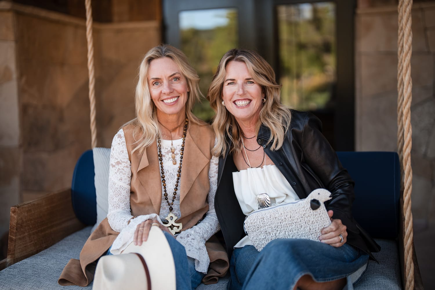 Two women sit together on a blue upholstered bench in a rustic architectural setting, framed by r... — Casey Addason Photography