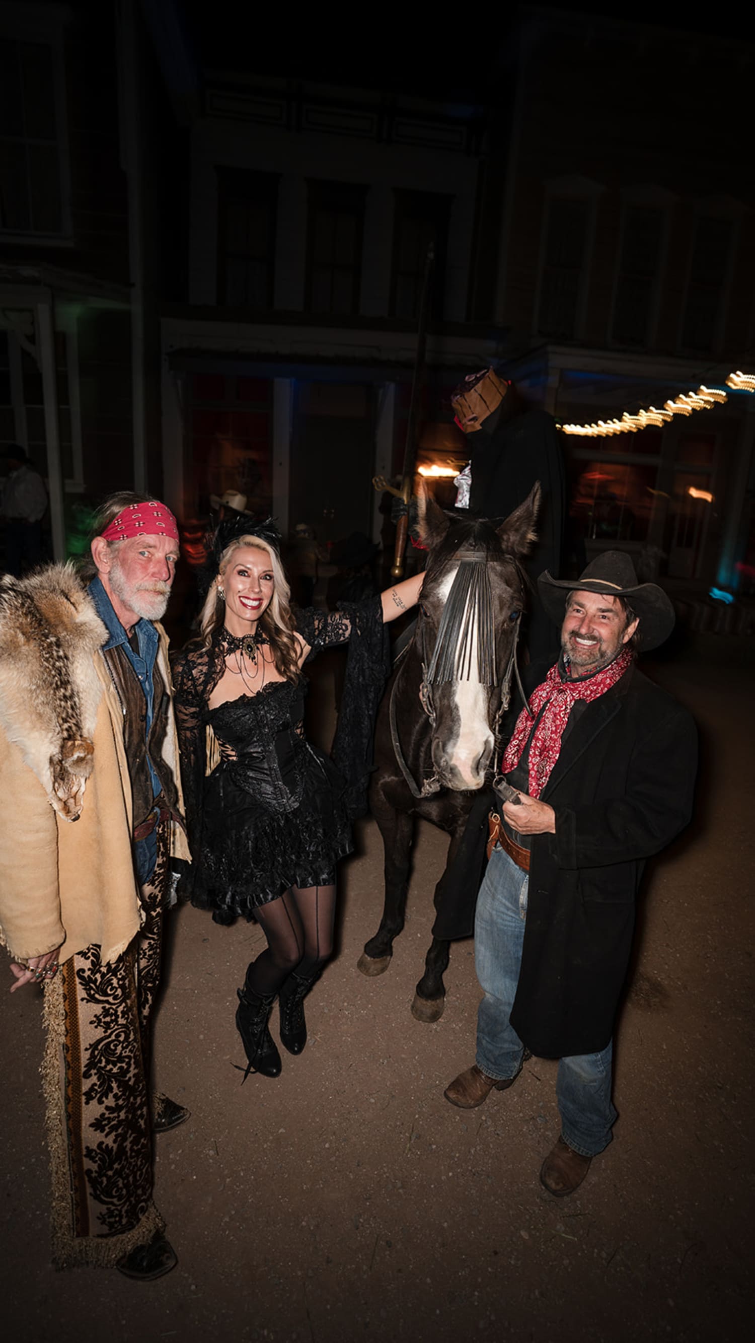 nighttime outdoor event captures four guests posing with a saddled horse in front of an adobe or ... — Casey Addason Photography