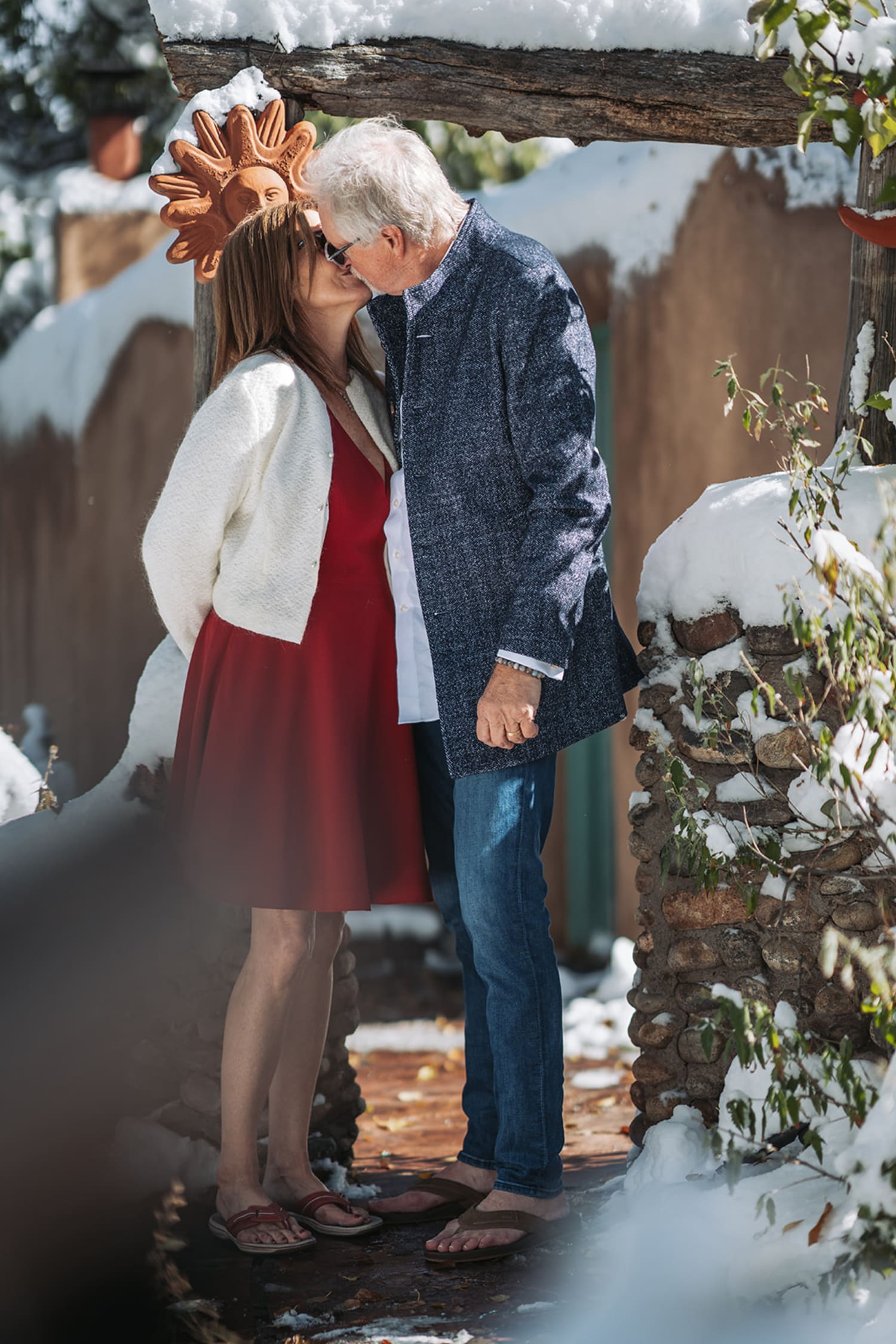 portrait captures a couple sharing a kiss beneath a rustic wooden pergola in a snow-dusted garden... — Casey Addason Photography
