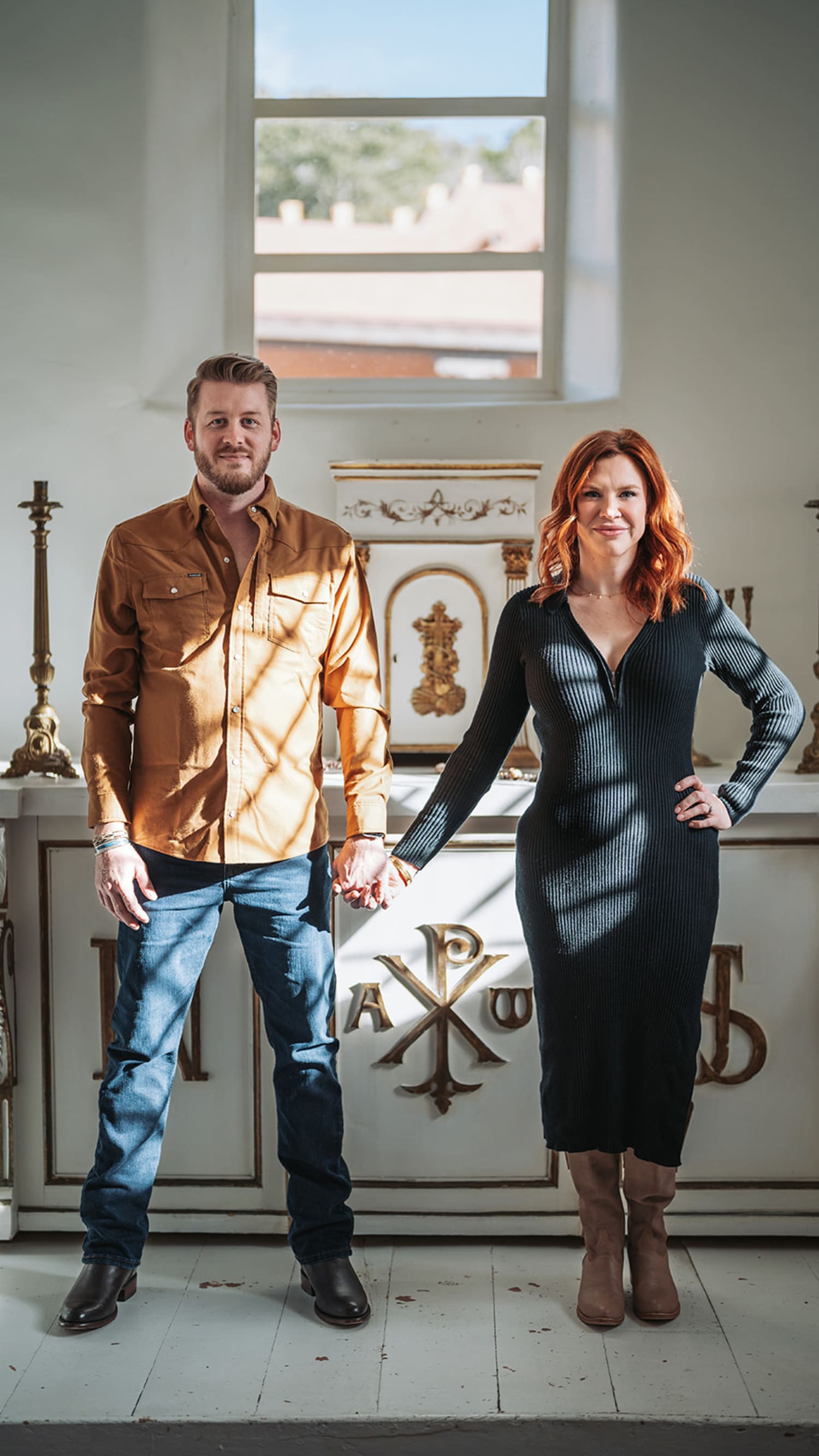Couple in traditional church interior with Chi-Rho symbol, man in metallic gold shirt, woman in black midi dress, Santa Fe, Casey Addason Photography