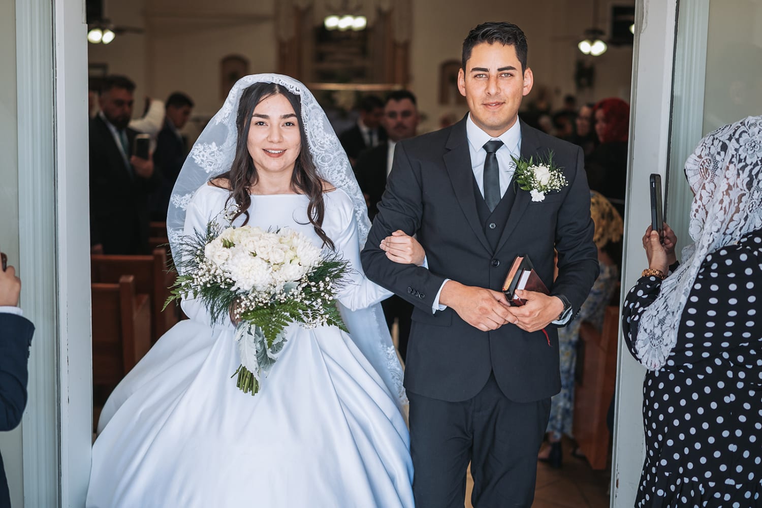photograph documents a bride and groom exiting through the doorway of an indoor church or chapel v... — Casey Addason Photography