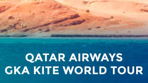 Leijasurffaaja keskellä ilmaa sinisen veden ja kallioisten aavikkokallioiden yläpuolella, tekstissä lukee Qatar Airways GKA Kite World Tour.