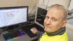 Mies keltaisissa turvaliiveissä työskentelee tietokoneella, jonka näytöllä on rakennuspiirustuksia.