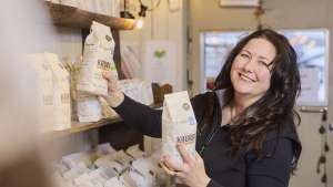 Hymyilevä nainen järjestelee jauho- tai viljapusseja kaupan hyllyillä.