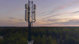 Matkapuhelinmasto metsän yllä auringonlaskun aikaan, taustalla värikäs taivas.