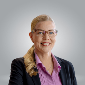 Mari Eklund. Hymyilevä vaaleahiuksinen nainen, jolla on silmälasit, vaaleanvioletti paita ja musta bleiseri.