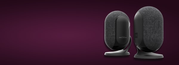 Kaksi modernia mustaa ja harmaata kangaspäällysteistä kaiutinta tummanruskealla pohjalla.