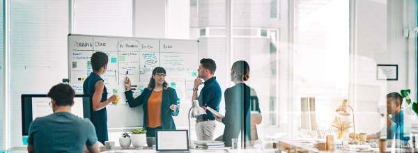 Ryhmä kollegoita tekee yhteistyötä ja pohtii ideoita valkotaululla modernissa toimistossa.