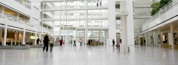 Tilava moderni atrium, jossa ihmiset kävelevät, valkoisten parvekkeiden ja lasiseinien ympäröimänä.