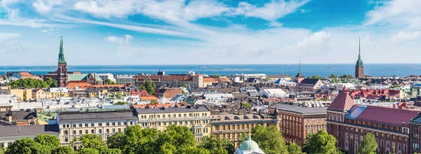 Ilmakuva Helsingistä vihreine puineen, historiallisine rakennuksineen ja Itämeren sinisen taivaan alla.