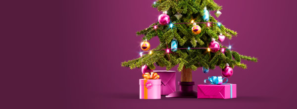 Joulukuusi, jossa on värikkäitä koristeita ja valoja, alla vaaleanpunaisia lahjoja ja rusetteja, violetilla taustalla.