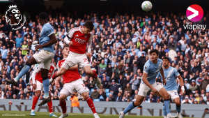 Arsenalin ja Manchester Cityn pelaajat hyppäävät päästämään palloa ruuhkaisessa jalkapallo-ottelussa stadionilla.
