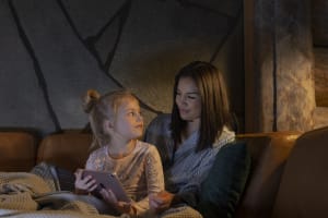 Nainen ja nuori tyttö istuvat yhdessä sohvalla hymyillen ja pitelevät tablettia viihtyisässä huoneessa.