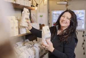 Hymyilevä nainen järjestelee jauho- tai viljapusseja kaupan hyllyillä.