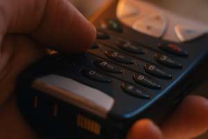 Lähikuva henkilöstä, joka valitsee numeroita mustalla matkapuhelimen näppäimistöllä.