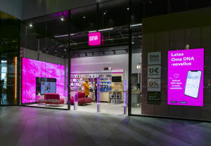 Värikäs DNA-myymälä, jossa on kirkkaan vaaleanpunaiset opasteet, puhelinnäytöt ja digitaalinen näyttö, jossa näkyy mobiilisovelluksen mainos.