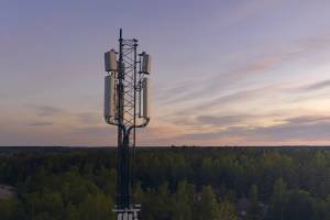 Matkapuhelinmasto metsän yllä auringonlaskun aikaan, taustalla värikäs taivas.