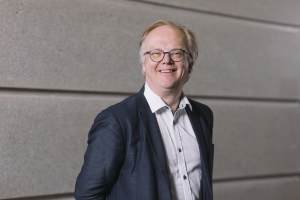 VTT:n Mika Rantakokko hymyilee harmaan seinän edessä ja katsoo kameraan