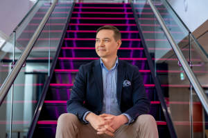 DNA:n teollisista ja tuotannollisista palveluista vastaava Business Line Lead Tapio Ranta istuu portaikossa katsoo sivulle ja hymyilee.