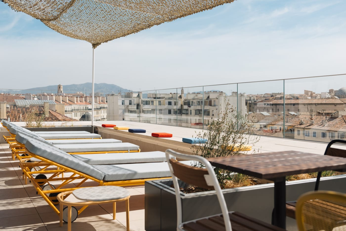 Yellow sun loungers and shade sail on the rooftop terrace of the Ruby Lilou hotel, facing the roofs of Marseille and the hills