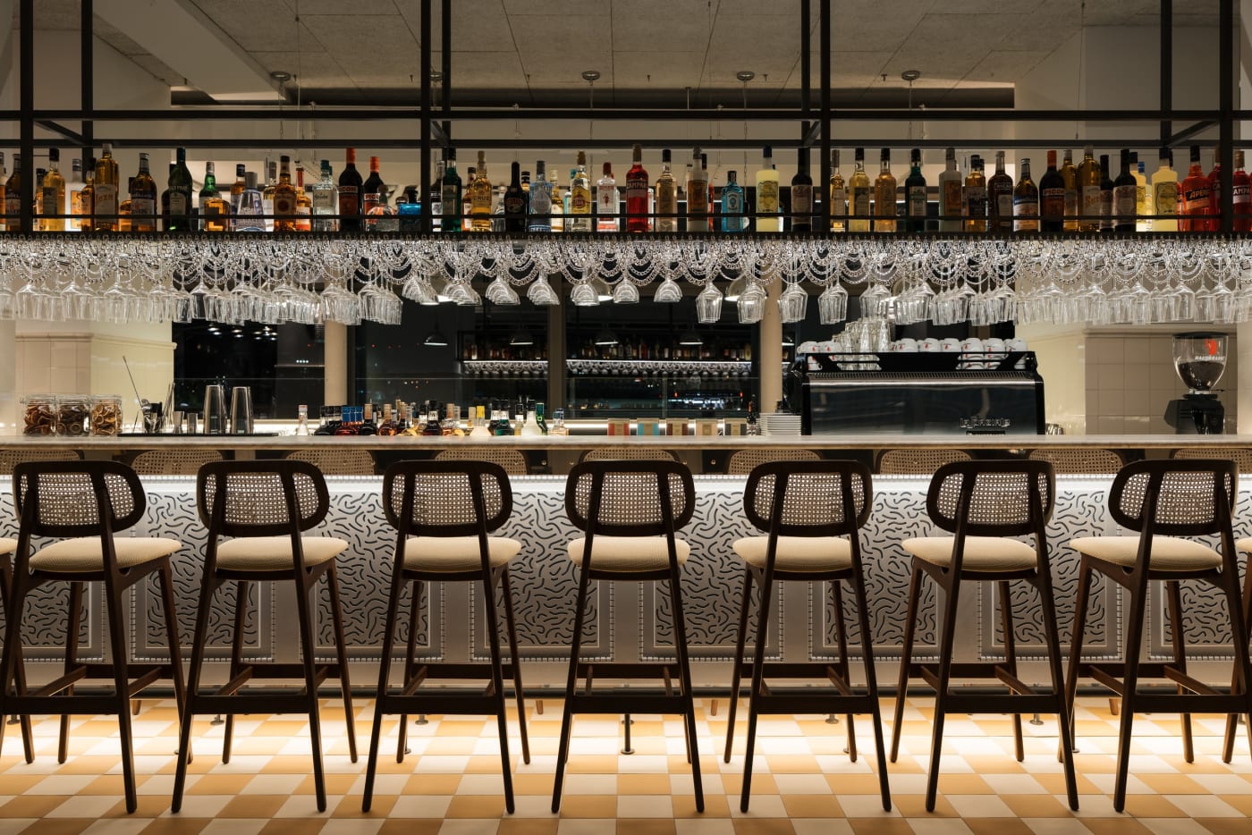 Bar counter of the Ruby Lilou hotel with wooden stools, checkerboard floor and shelf of bottles