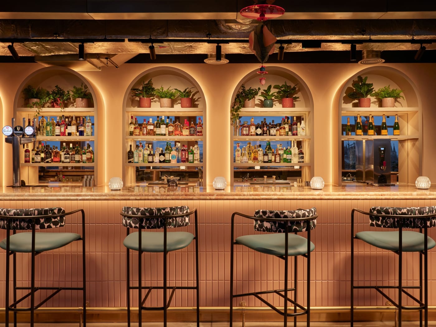 Le bar aux niches en arcades garnies de bouteilles et de plantes du Hotel Indigo Gloucester · The Forum